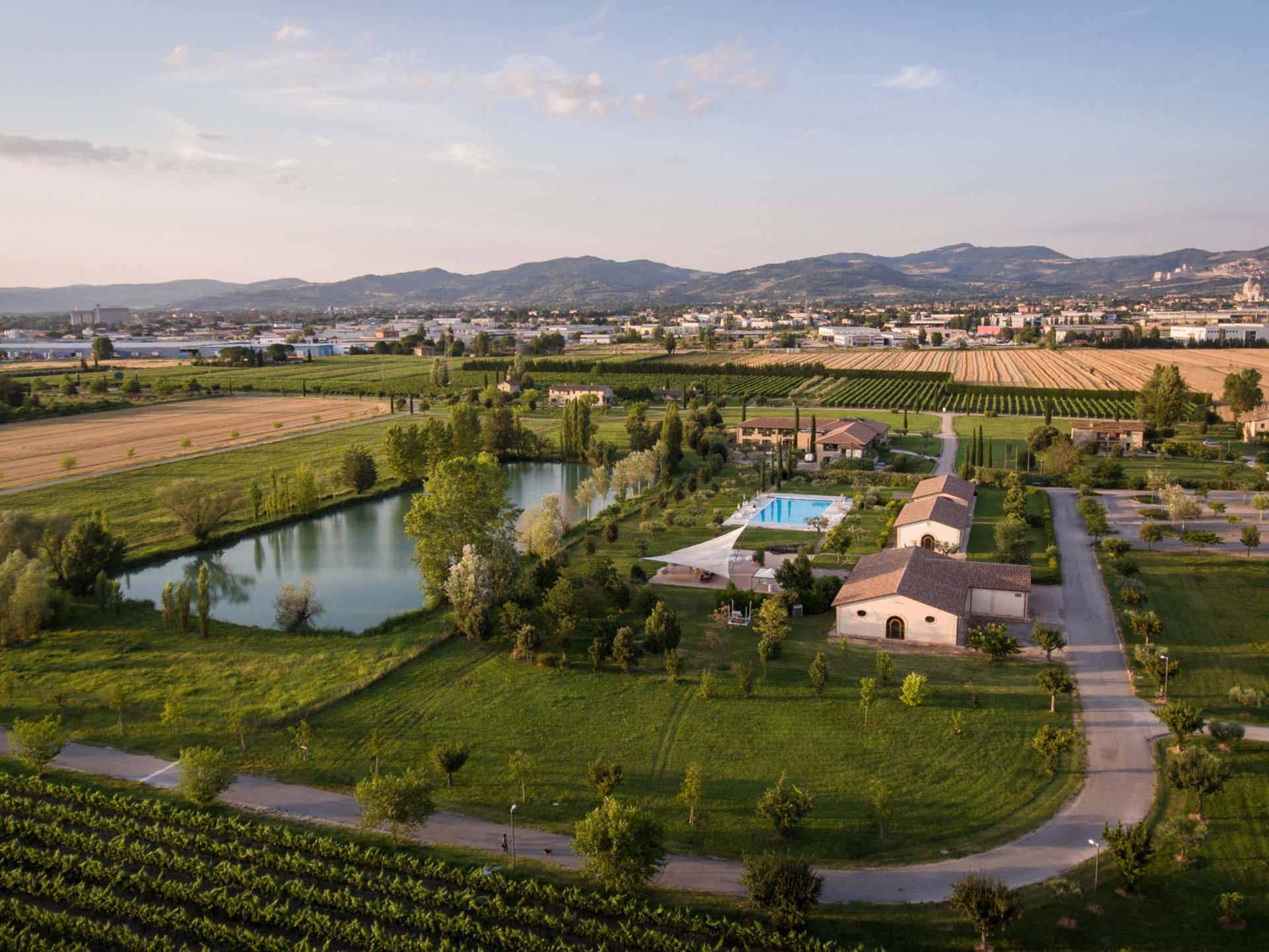A Santa Maria degli Angeli - Assisi ( Perugia ) Centro Congressi e Meeting d'eccezione? I tuoi eventi vista Assisi Umbria Veduta aerea di un agriturismo con piscina, laghetto e campi coltivati