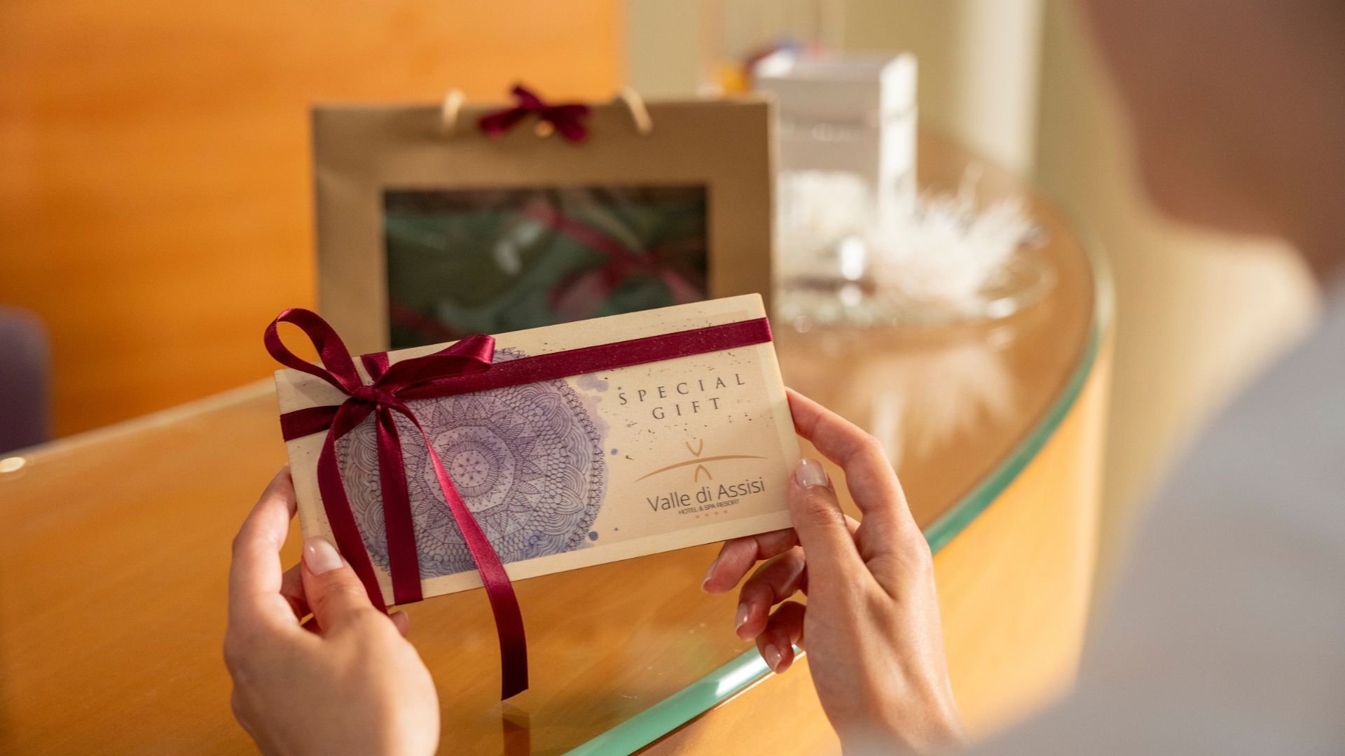 Italian Gift Voucher Valentine's Day and Anniversary Gift Ideas from spa wellness to massages with dinner. Hands hold a Valle di Assisi gift voucher decorated with a red ribbon