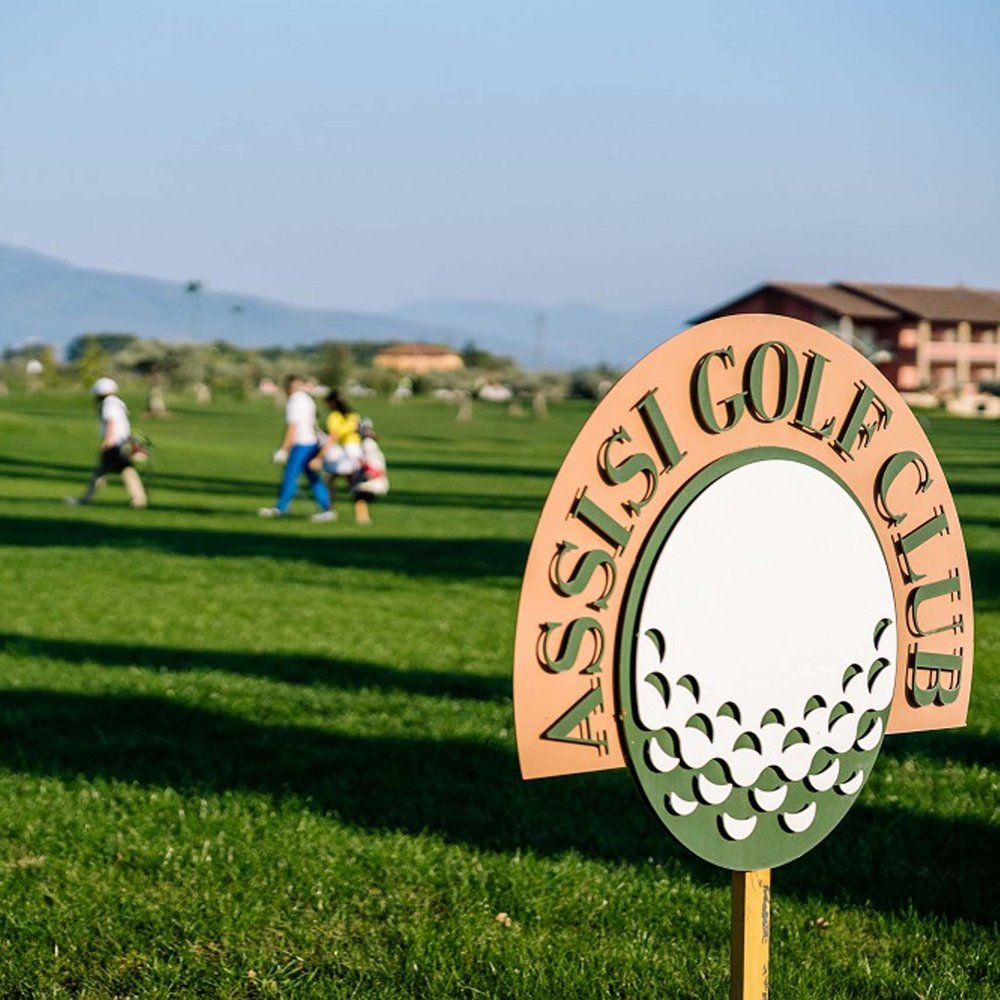 Urlaub in Umbrien? Und noch viel mehr! Schild des Assisi Golf Club auf Golfplatz mit Spielern im Hintergrund