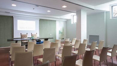 A Santa Maria degli Angeli - Assisi ( Perugia ) Centro Congressi e Meeting d'eccezione? I tuoi eventi vista Assisi Umbria Sala conferenze con sedie bianche e schermo di proiezione Valle di Assisi