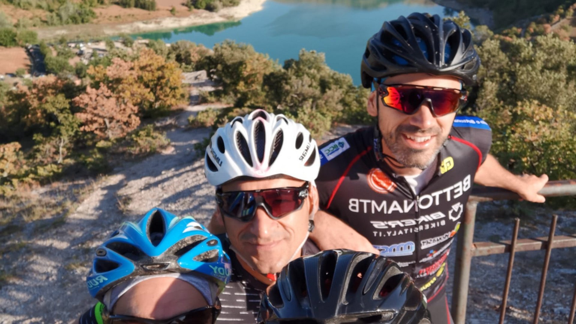 A holiday near Assisi: activities galore Four smiling cyclists wearing helmets in front of a mountain lake