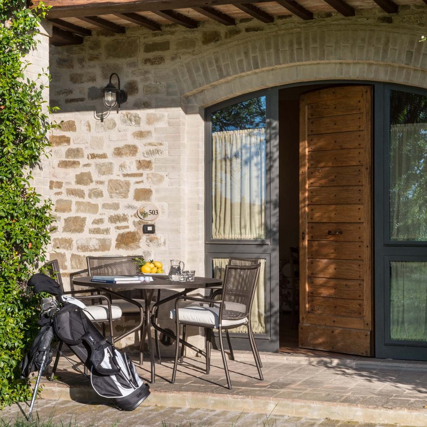 Resort bei Assisi im Country-Style Veranda mit Tisch und Stühlen, Golfbag lehnt, halb geöffnete Holztür