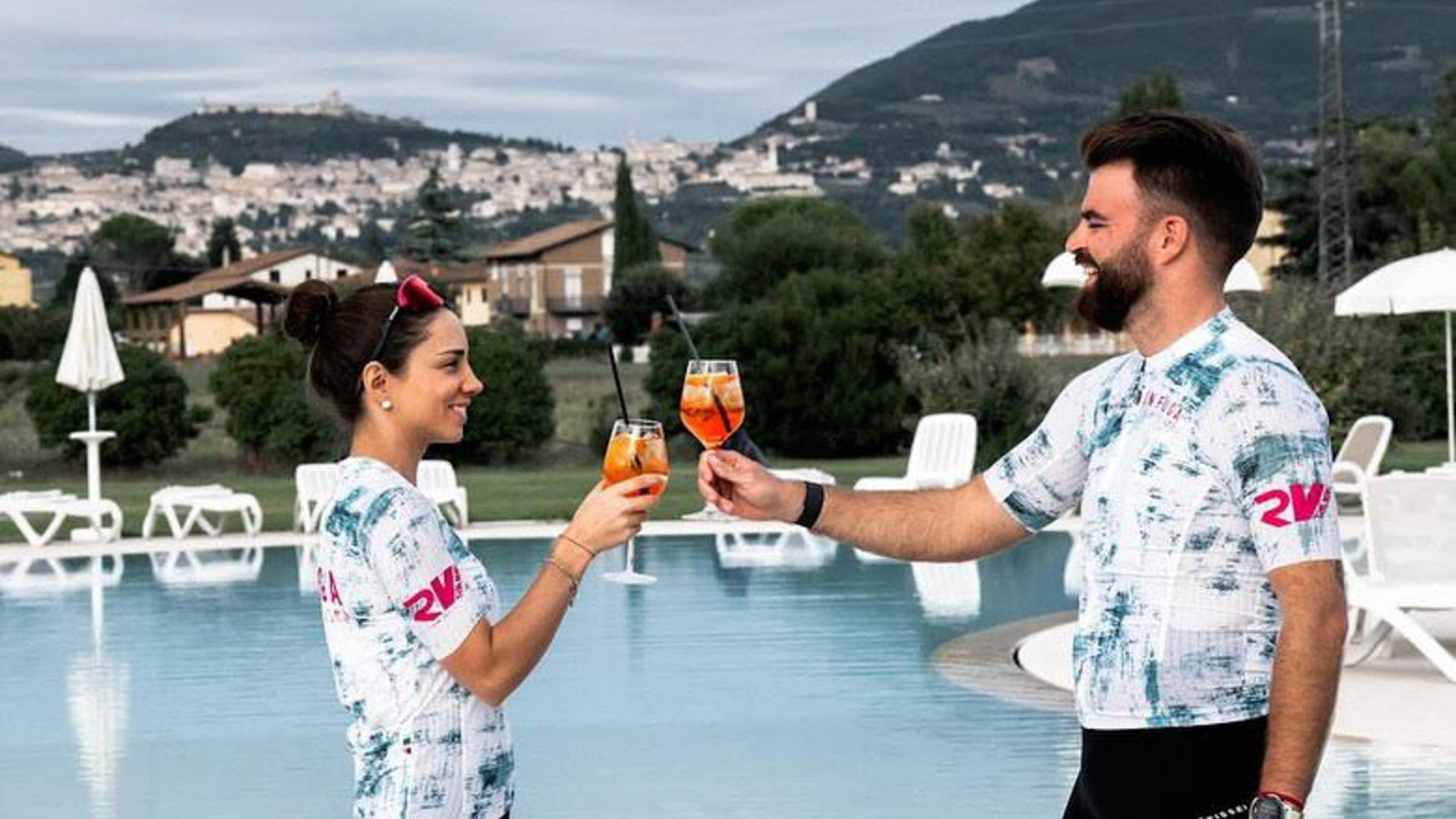 A holiday near Assisi: activities galore Two people toasting with cocktails by an outdoor pool with hills in the background