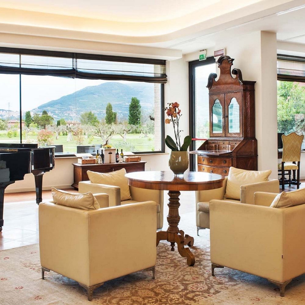 A hotel for families in Umbria with that little extra Elegant living room with beige armchairs, round table, piano, and mountain view