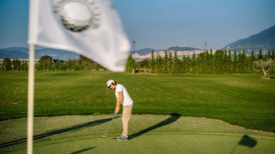 Perugia ha un Centro Meeting e Congressi d'eccezione: ai piedi di Assisi in Umbria Golfista che gioca un putt su un green al tramonto con bandiera sventolante.