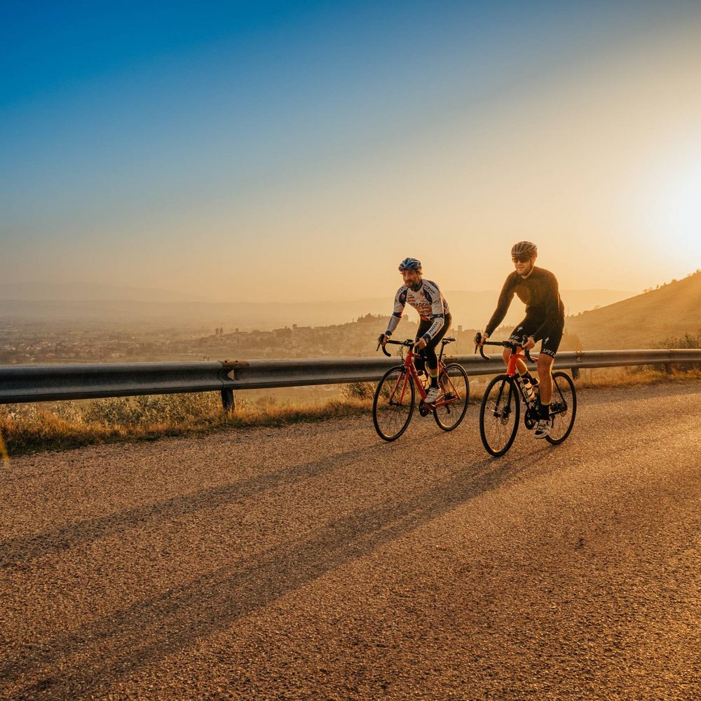 Vacanze in Umbria, vacanze di pienezza Due ciclisti su strada al tramonto in una zona collinare.