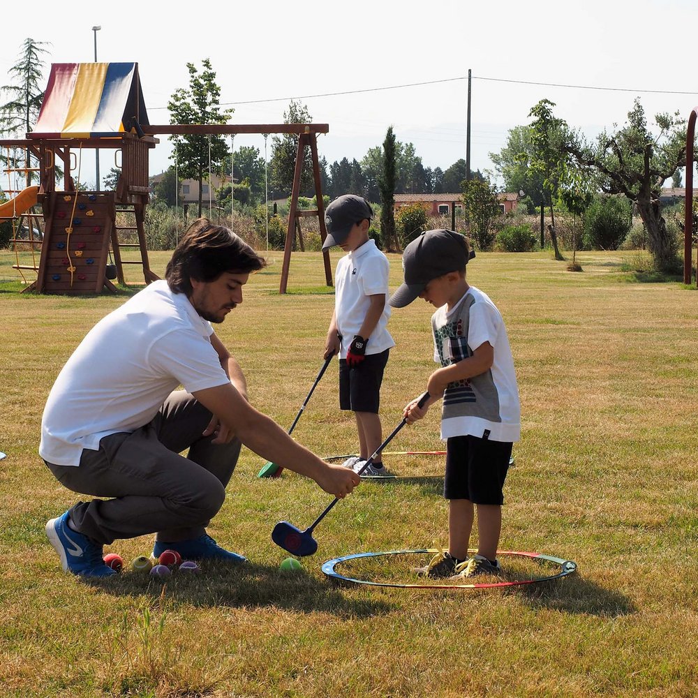 Valle di Assisi, ein Hotel für Familien mit Kindern Mann bringt zwei Kindern im Freien das Golfspiel bei