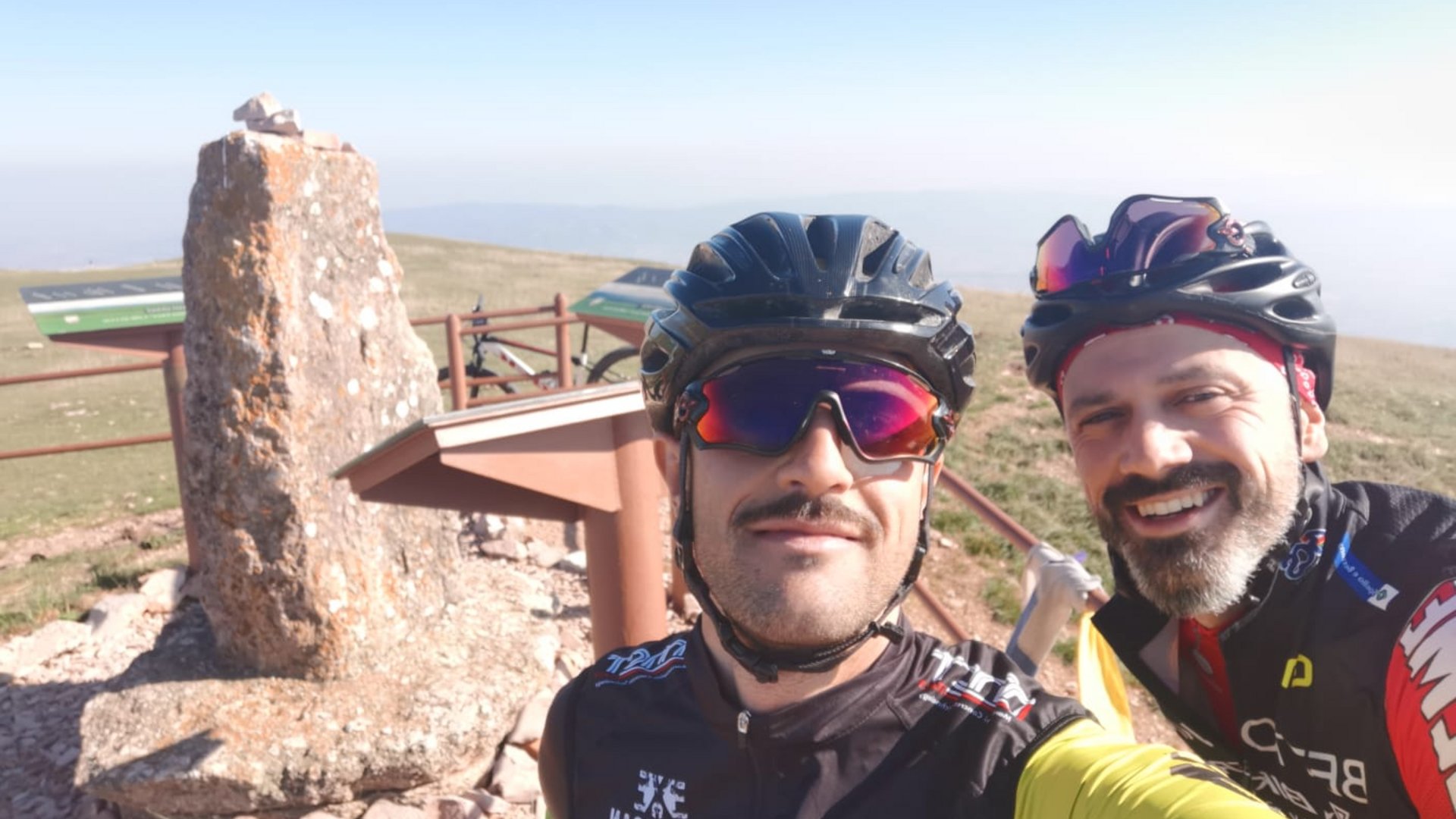 A holiday near Assisi: activities galore Two cyclists wearing helmets smiling in front of a stone and information boards on a mountain