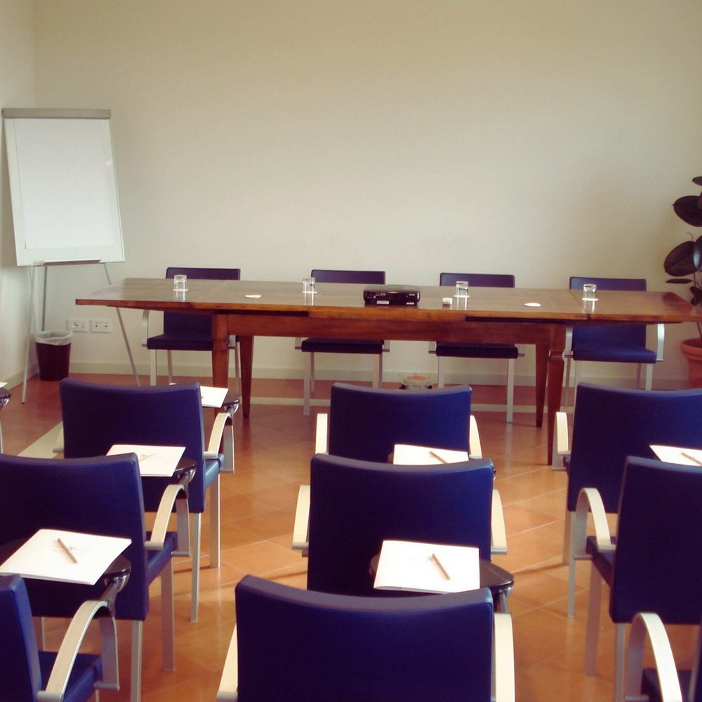 I vostri Incontri Aziendali a Perugia, Assisi Umbria Aula conferenze con sedie blu e tavolo con bicchieri e lavagna a fogli mobili
