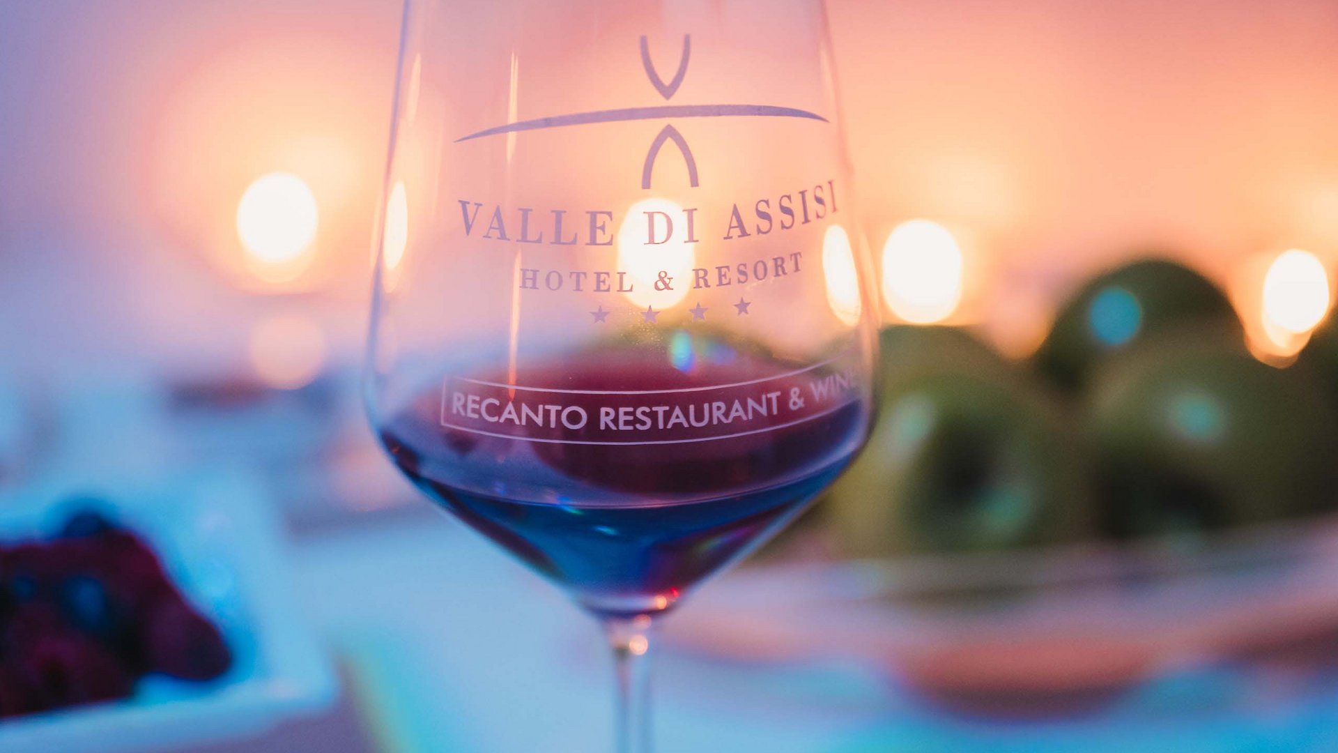 Guida Completa alle nostra Spa in Umbria: le migliori offerte di coppia, pacchetti e Day SPA, offerte benessere lastminute. Calice di vino rosso con logo Valle di Assisi Hotel e Resort e candele sullo sfondo