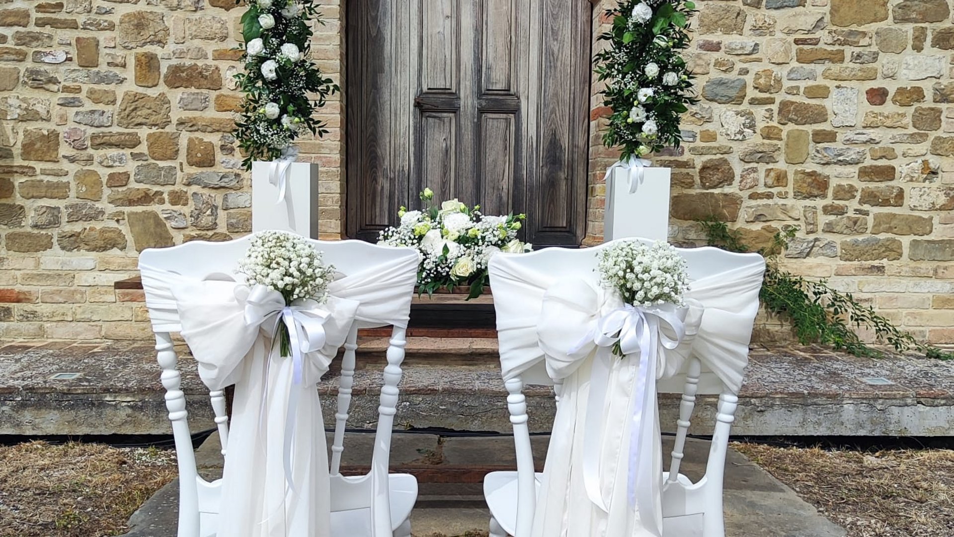 Valle di Assisi: un resort per matrimoni ad Assisi Due sedie bianche decorate con fiori e nastri davanti a un arco floreale