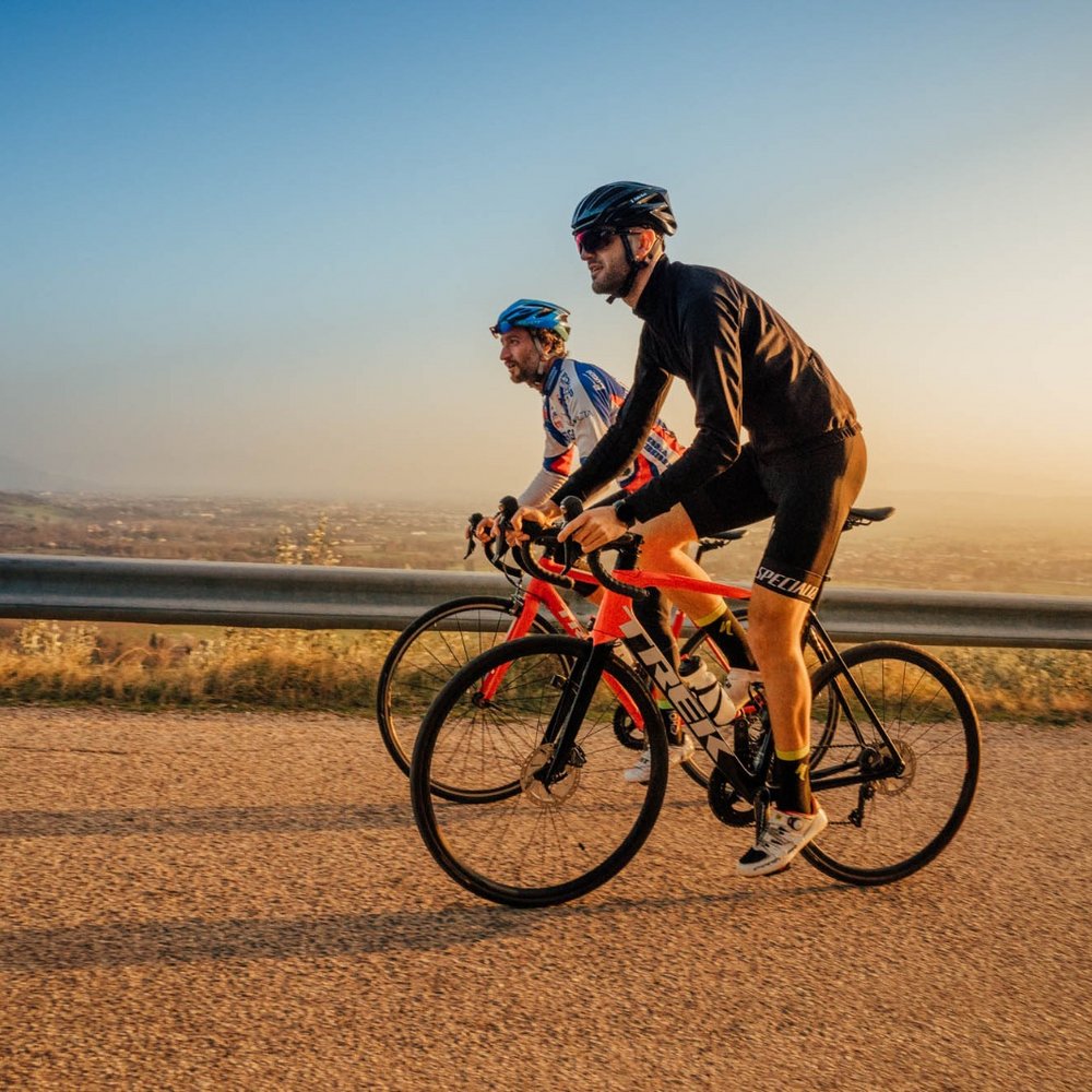 A holiday near Assisi: activities galore Two cyclists riding on a hilly road at sunset wearing cycling gear