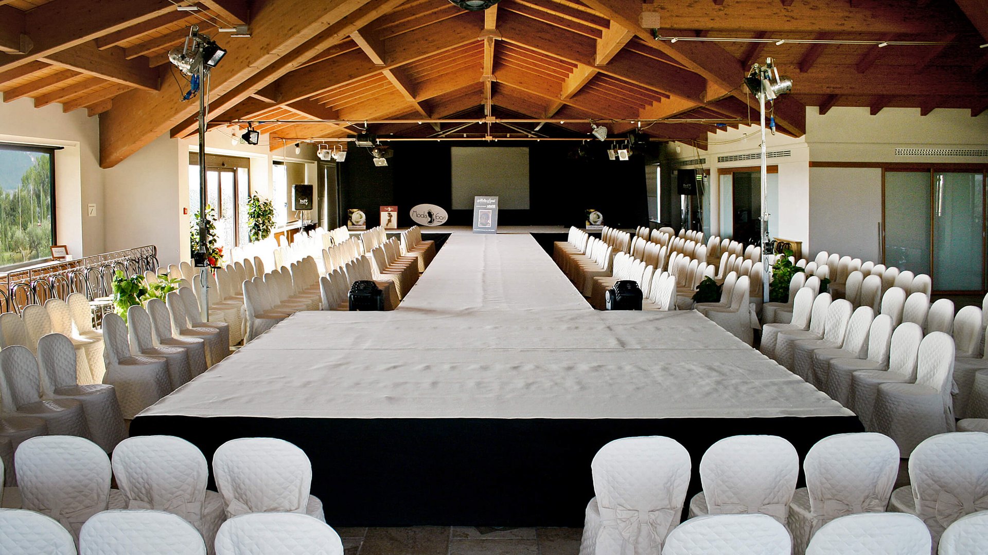A Santa Maria degli Angeli - Assisi ( Perugia ) Centro Congressi e Meeting d'eccezione? I tuoi eventi vista Assisi Umbria Passerella per moda vuota con sedie coperte di bianco in sala con soffitto in legno