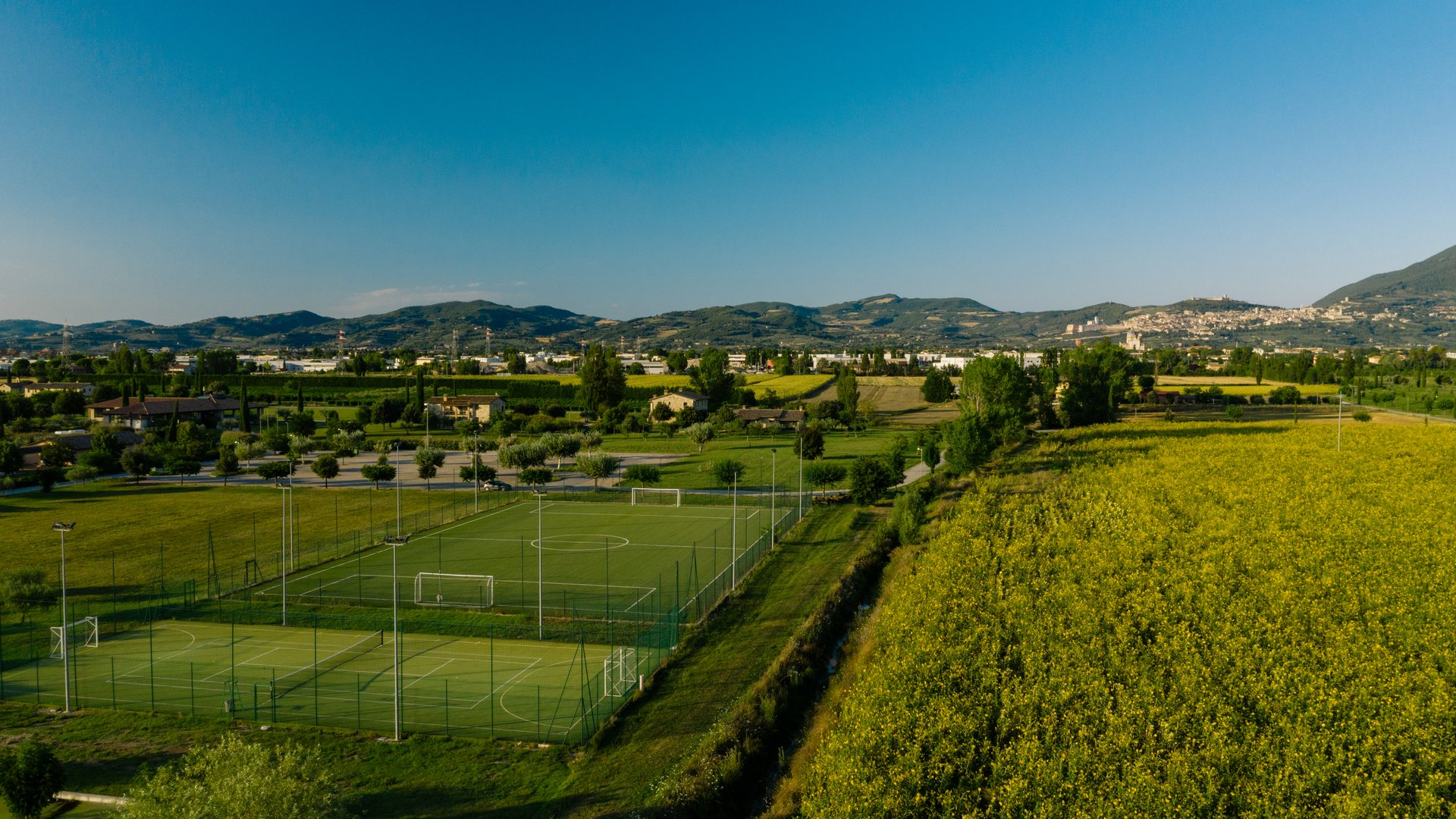A holiday near Assisi: activities galore Green soccer fields next to a yellow field with hills in the background