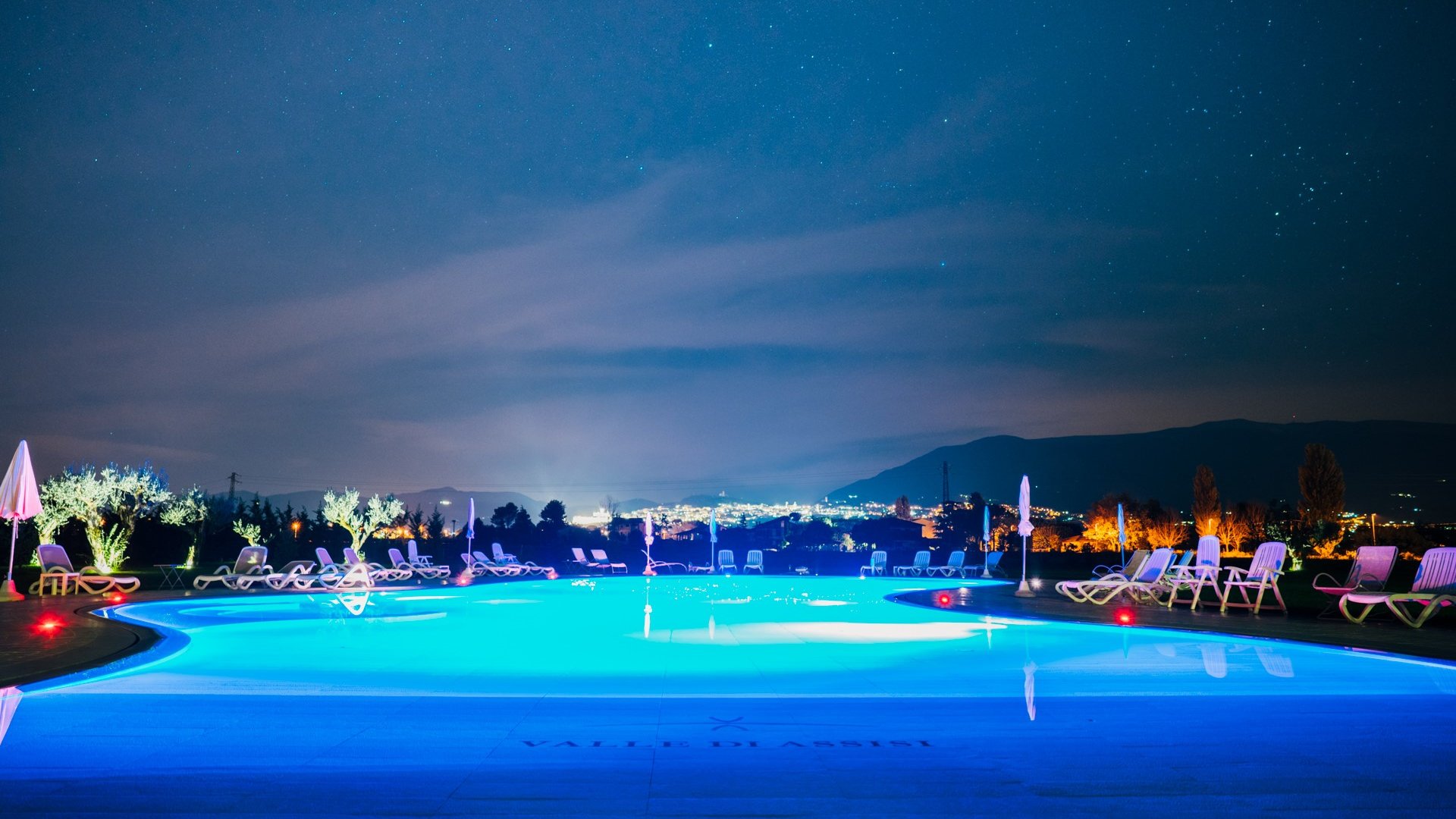 Hotel a 10 minuti di macchina da Assisi e la Basilica di San Francesco e il suo centro storico, 3 minuti di macchina dalla Porziuncola Piscina illuminata di blu di notte con lettini e ombrelloni intorno