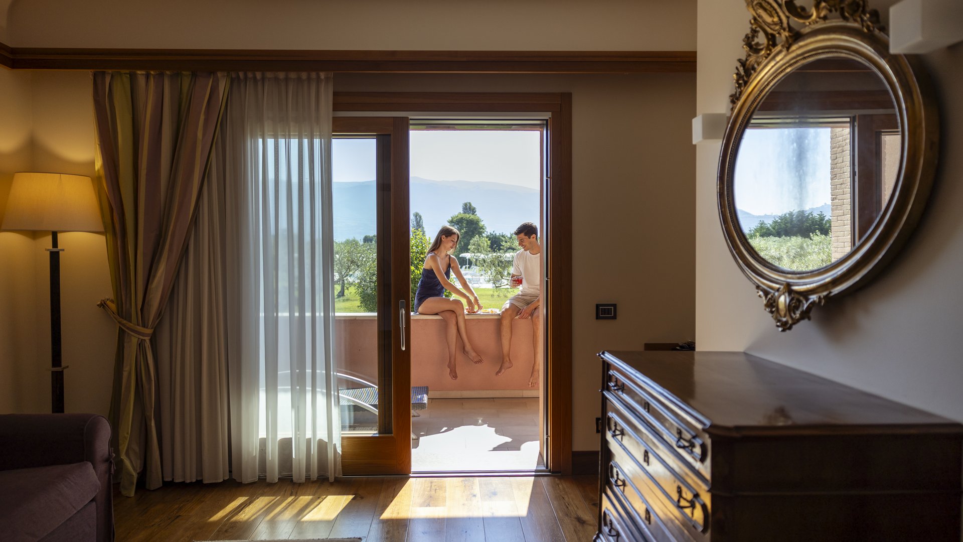 Italian Gift Voucher Valentine's Day and Anniversary Gift Ideas from spa wellness to massages with dinner. Elegant room with two people seated on the balcony overlooking greenery and hills