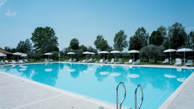 Perugia ha un Centro Meeting e Congressi d'eccezione: ai piedi di Assisi in Umbria Piscina all'aperto con lettini bianchi e ombrelloni in un giardino soleggiato