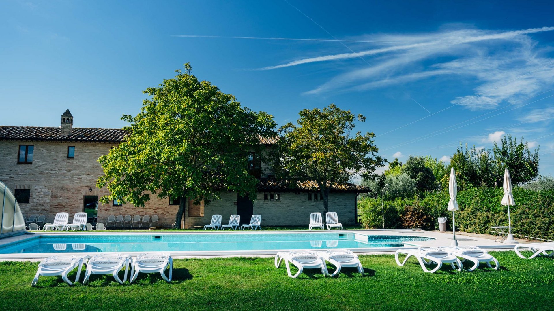 Urlaub in Umbrien? Und noch viel mehr! Außenpool mit Liegestühlen und Sonnenschirmen in einem sonnigen Garten vor einem Haus