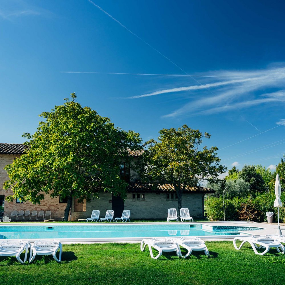 Ferienhaus in Umbrien mit Pool: in unserem Resort Außenpool mit Liegestühlen und Sonnenschirmen in einem sonnigen Garten vor einem Haus