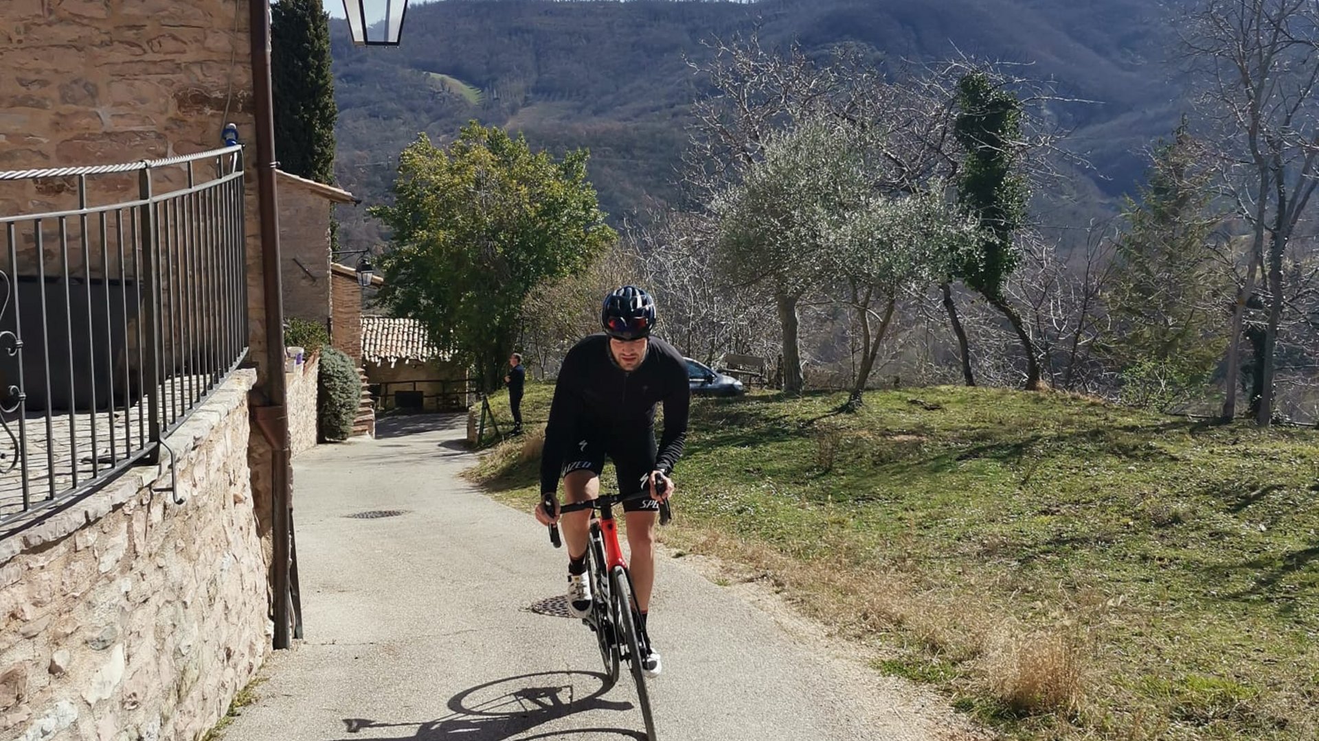 A holiday near Assisi: activities galore Cyclist in black gear riding uphill near stone house and hills