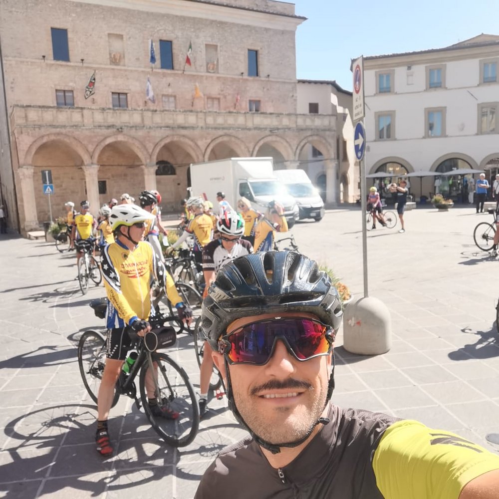 Fabio Bike Manager in tour con amanti bike in Umbria Gruppo di ciclisti in abbigliamento sportivo in piazza storica soleggiata