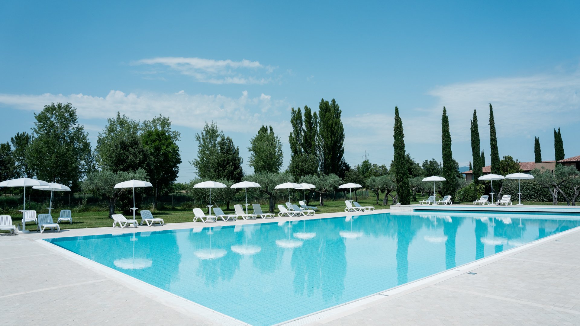A holiday near Assisi: activities galore Outdoor swimming pool with white lounge chairs and umbrellas in a garden