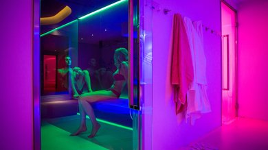 Your spa near Assisi: Assisi Cantico Spa Two people sitting in a sauna with colorful lighting and towels hanging on the wall