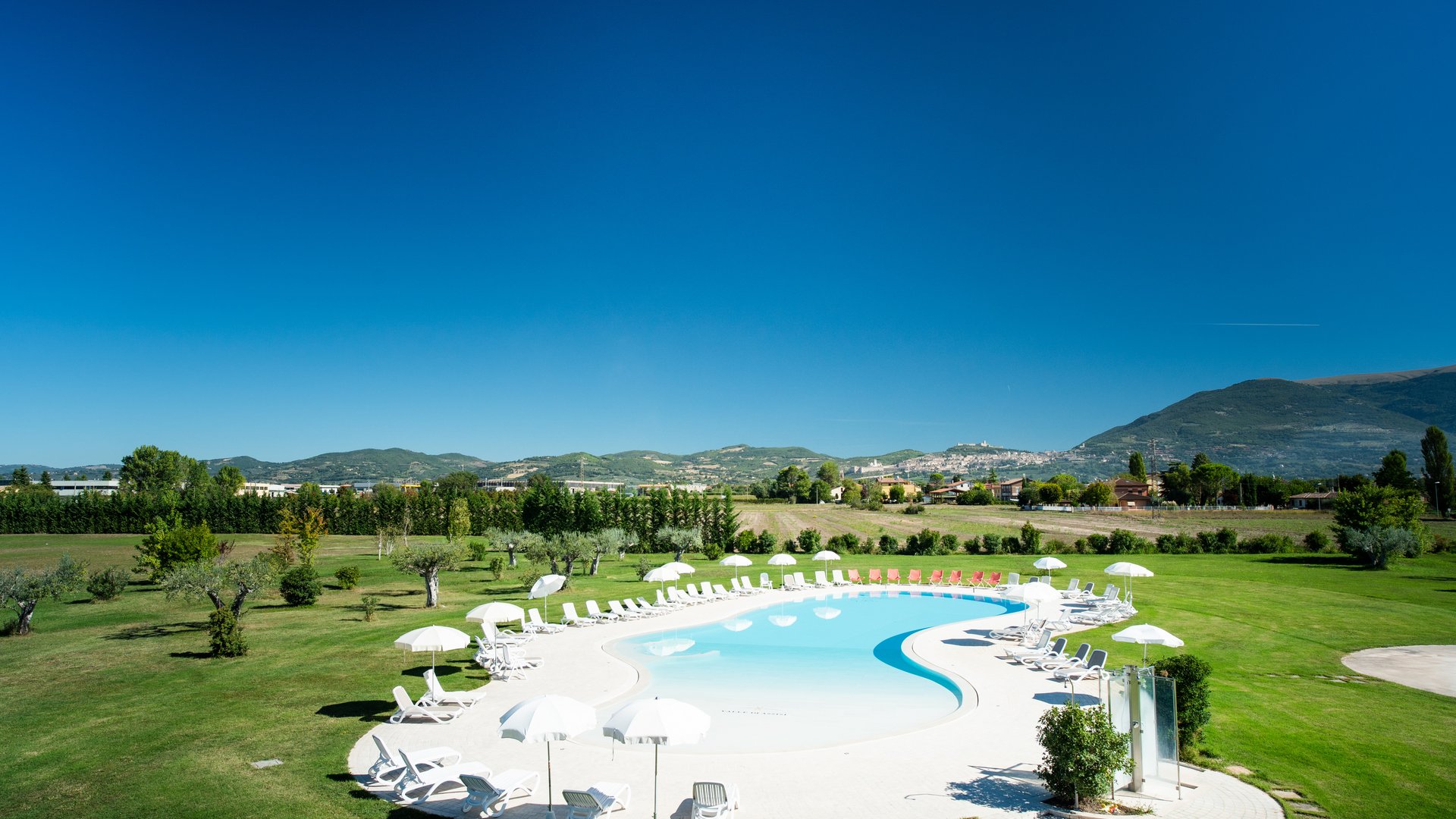A holiday near Assisi: activities galore Bean-shaped swimming pool with white loungers and umbrellas on green lawn