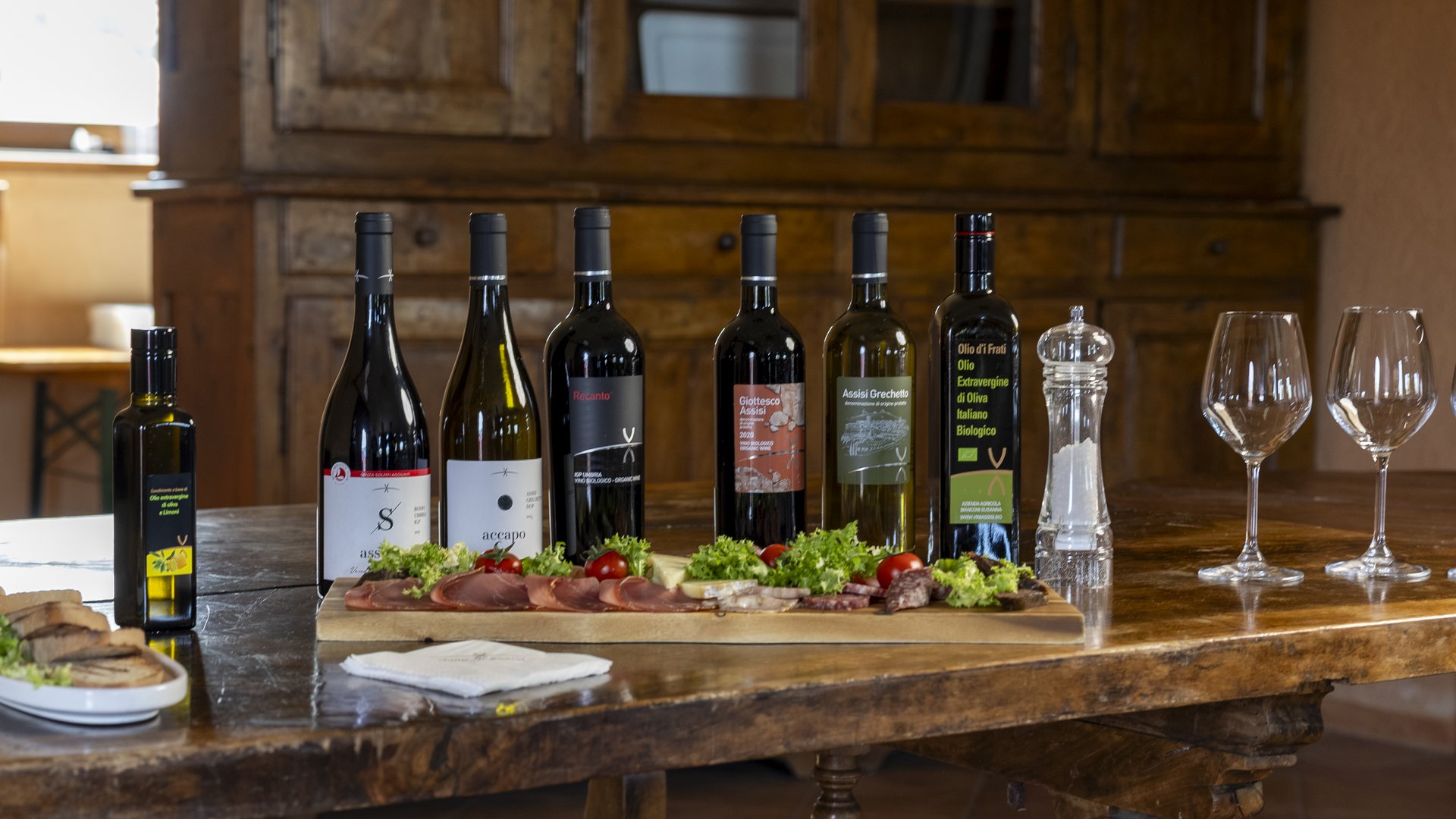 Un hotel vicino ad Assisi con mezza pensione da sogno Bottiglie di vino, olio e tagliere con salumi e verdure su tavolo di legno
