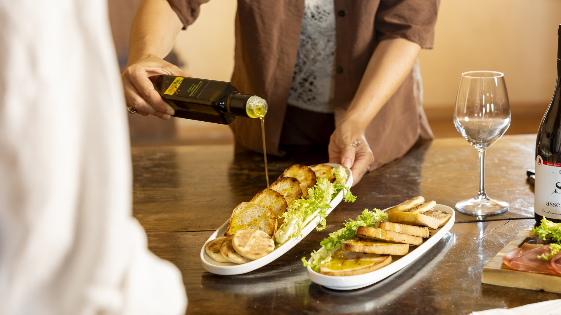 Discover our farm in Umbria. Person pouring olive oil on toasted bread slices with lettuce on white plates