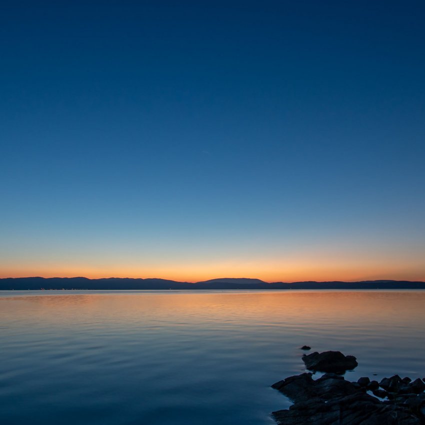 Quanto Dista Valle di Assisi Hotel Resort? Tramonto sul lago con cielo limpido e riflessi sull'acqua calma