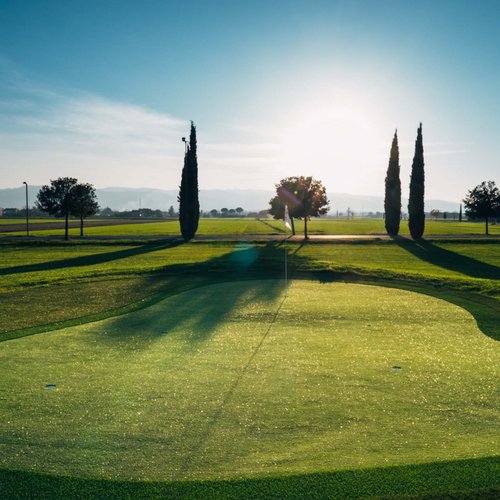 Die Mission des Valle di Assisi Golfplatz bei Sonnenuntergang mit Bäumen und tiefstehender Sonne