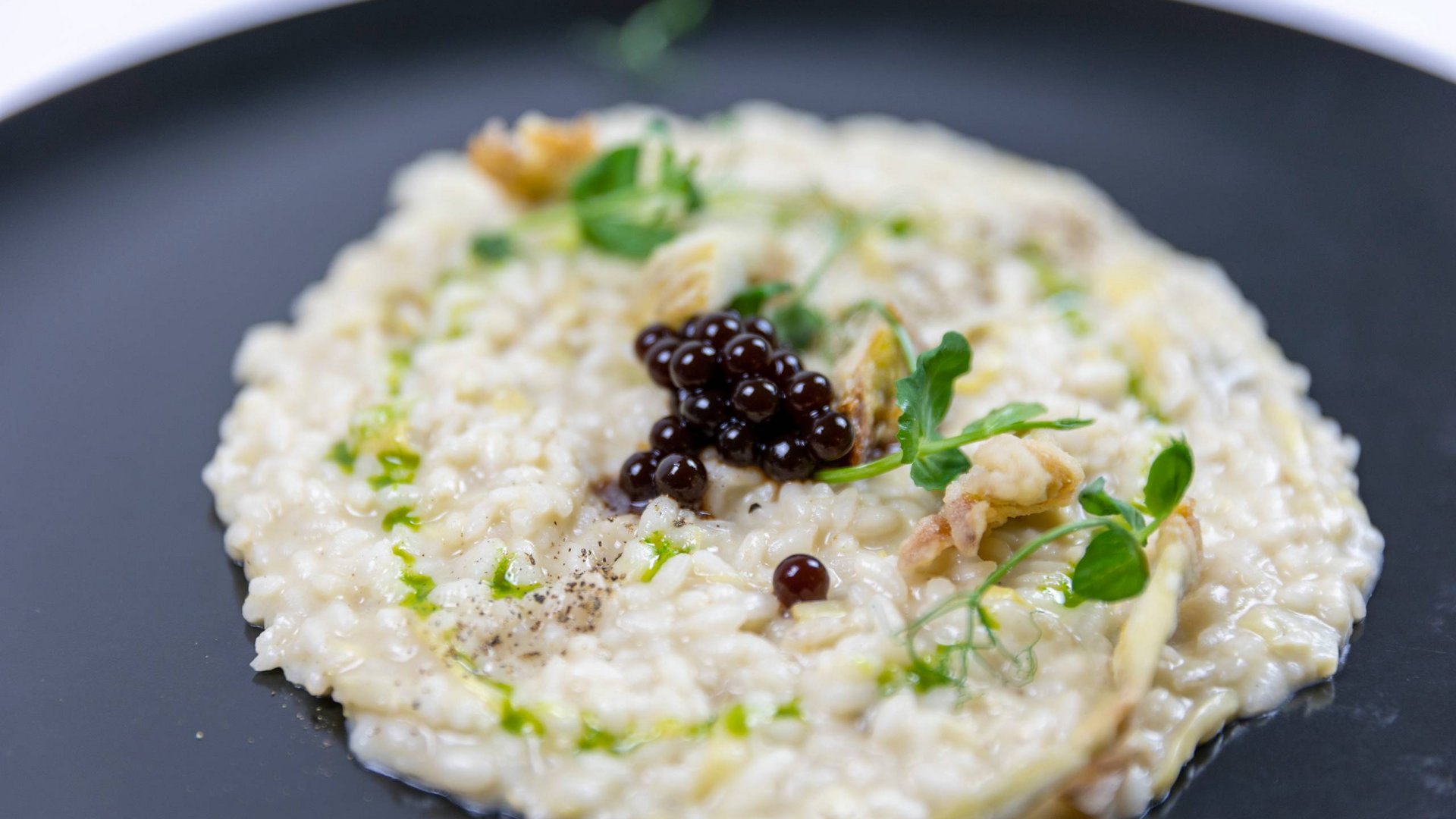 Umbrien: Unterkunft mit Restaurant Cremiges Risotto mit schwarzen Gelkügelchen und frischen Kräutern auf schwarzem Teller