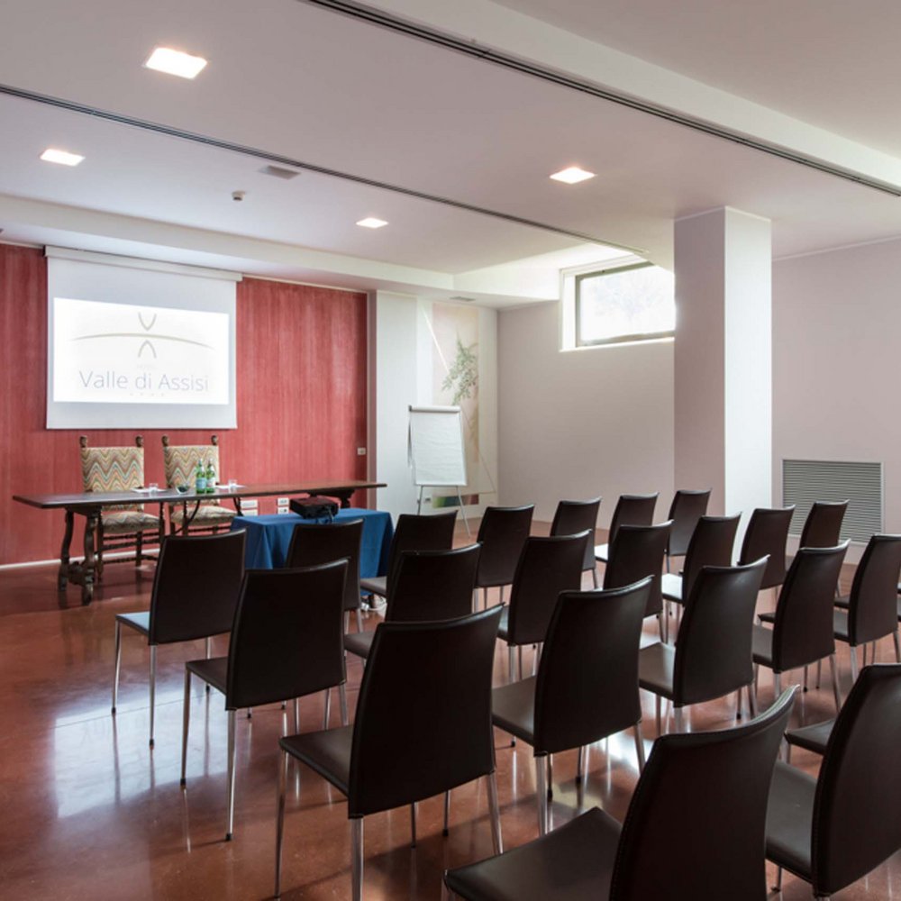 Ihr Kongresszentrum in Umbrien Konferenzraum mit Stühlen in Reihen und Tisch mit zwei Stühlen vor einer Leinwand