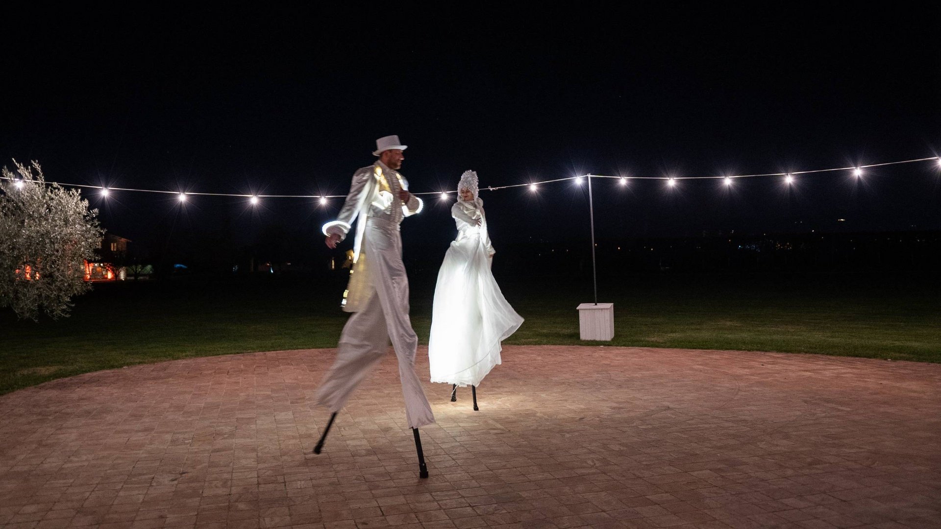 Your wedding location in Assisi Two performers on stilts in white costumes illuminated outdoors at night