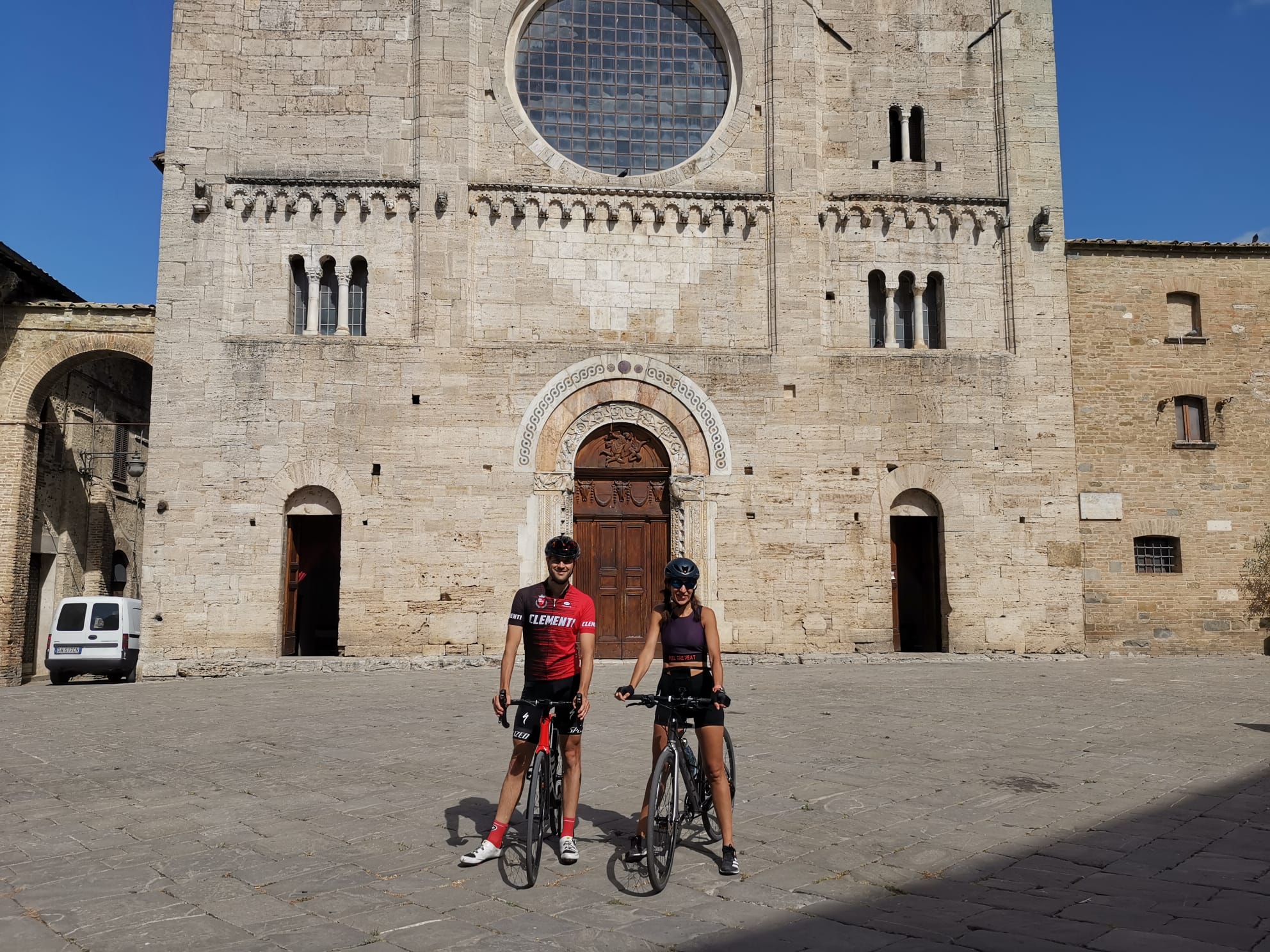 A holiday near Assisi: activities galore Two cyclists with bikes in front of a historic stone church in sunlight